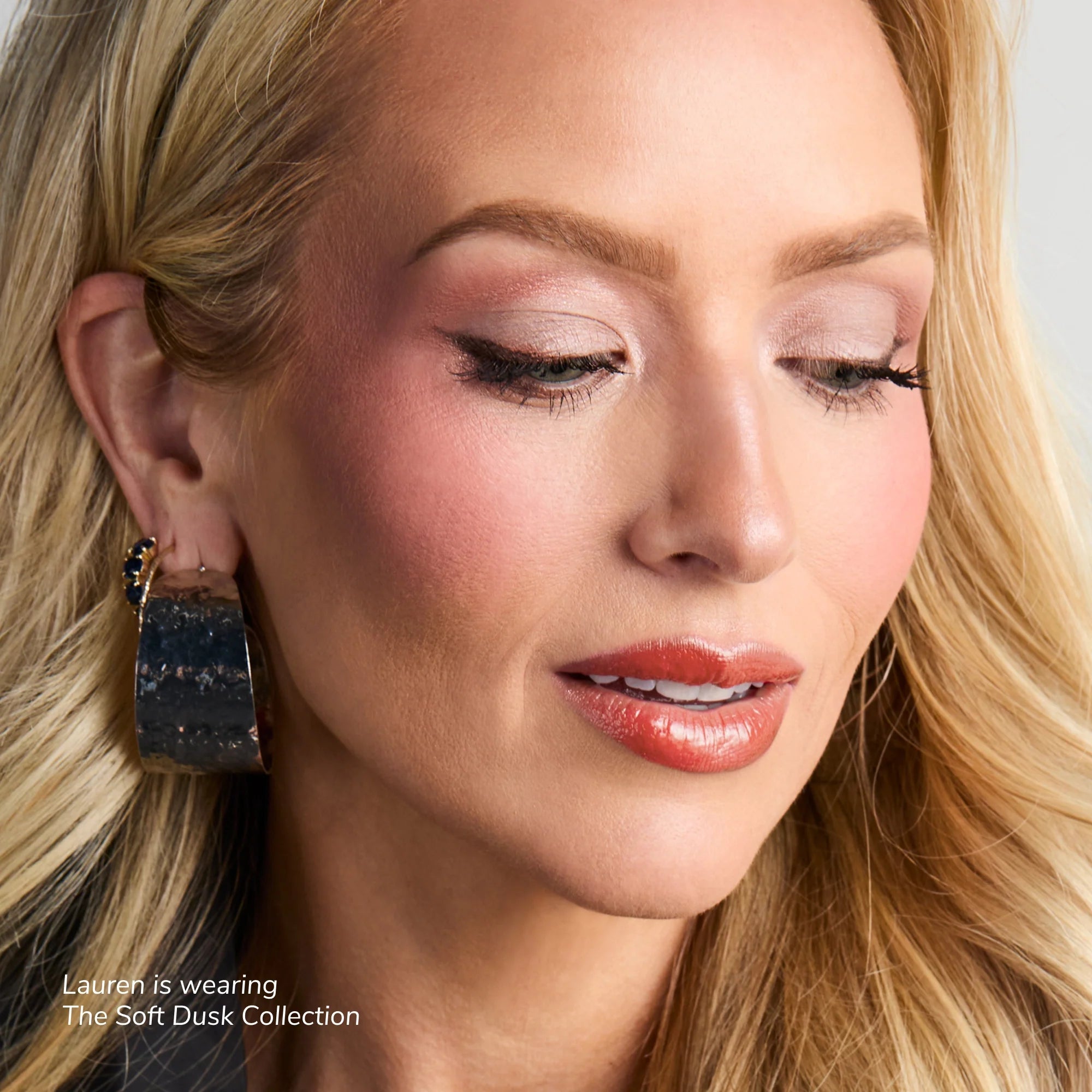 Close up of a woman wearing The Soft Dusk Collection makeup with pink eyeshadow and peach glossy lips.
