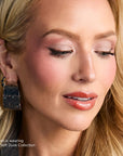 Close up of a woman wearing The Soft Dusk Collection makeup with pink eyeshadow and peach glossy lips.
