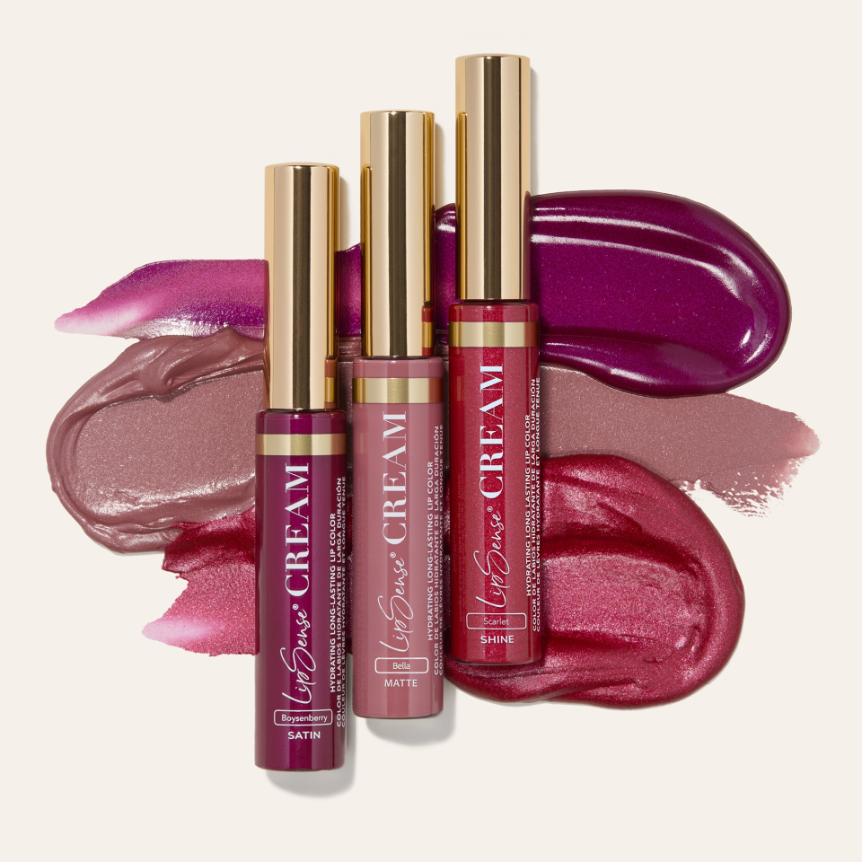 Assorted lip gloss tubes with gold caps over pink and purple lipstick swatches