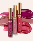 Assorted lip gloss tubes with gold caps over pink and purple lipstick swatches