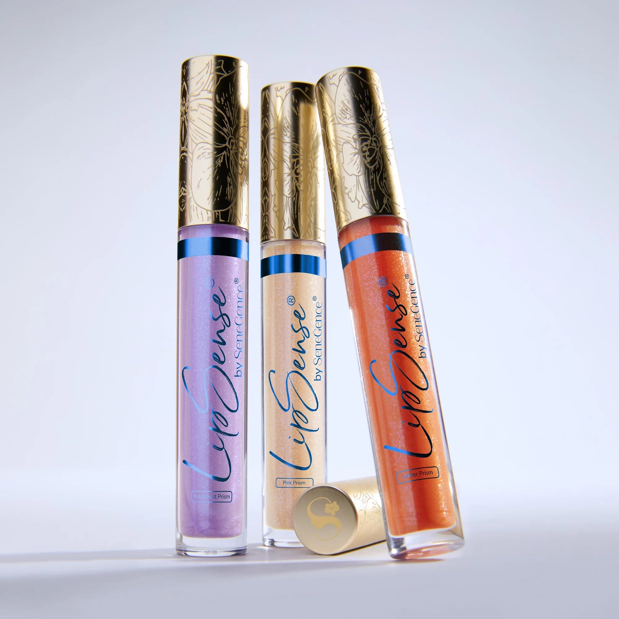 Three LipSense Prismatic gloss tubes with ornate gold caps standing upright.